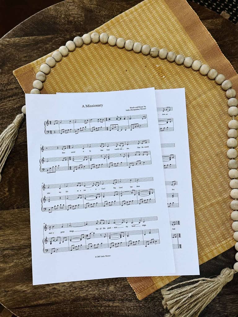 Sheet music for the song "A Missionary" by Lois and India sitting on a table top with a bead strand and placemat.