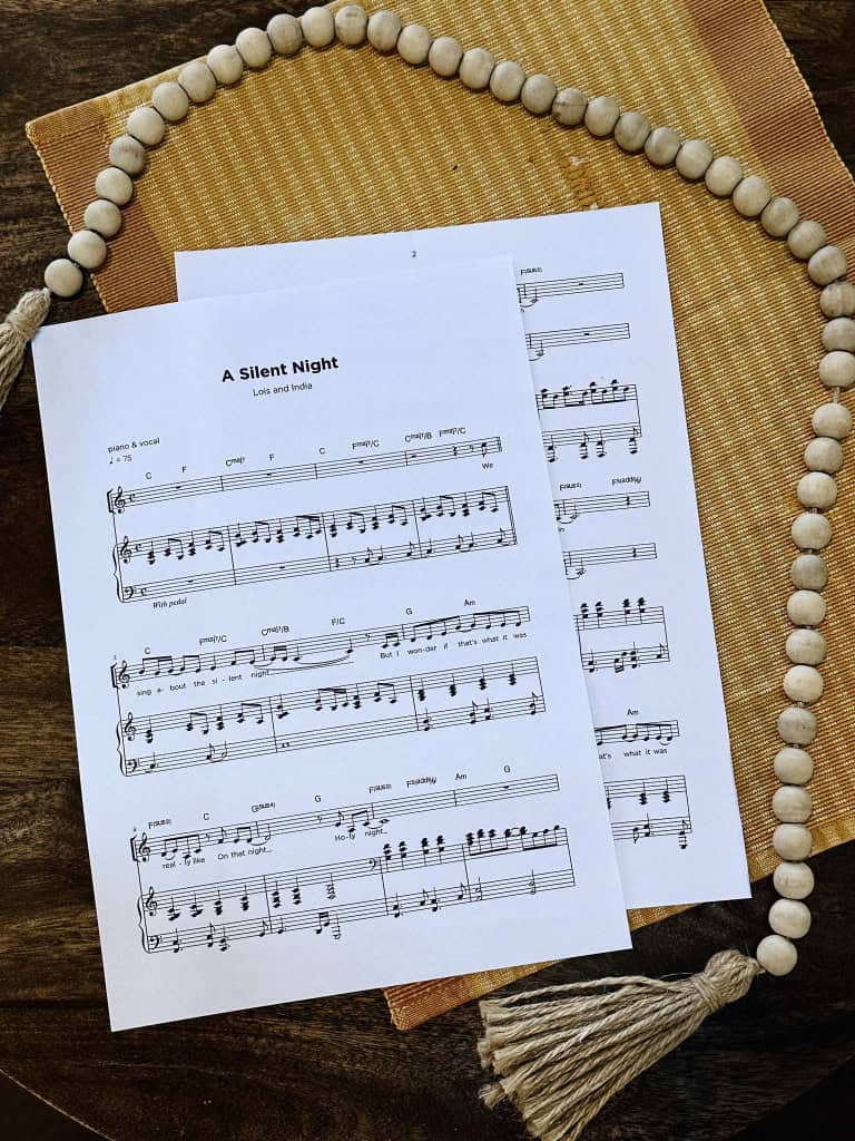 Sheet Music for "A Silent Night" by Lois and India laying on a table with a beige placemat and a strand of beads.