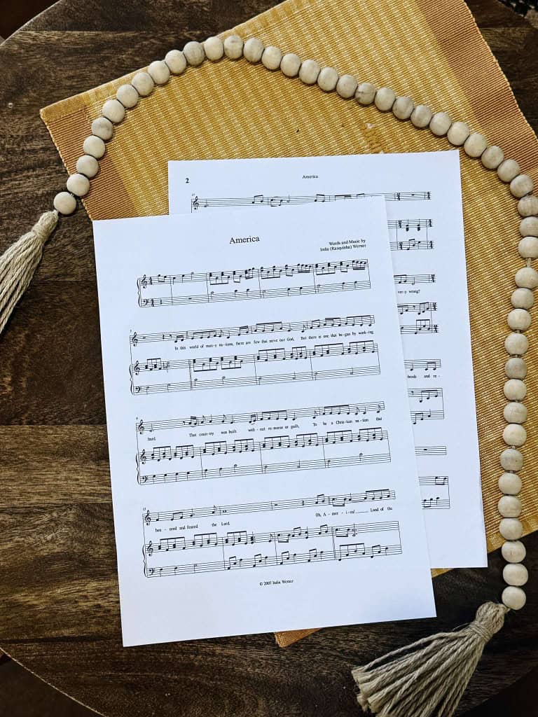 Sheet music for "America" By Lois and India laying on a table with a beige placemat and a string of beads.