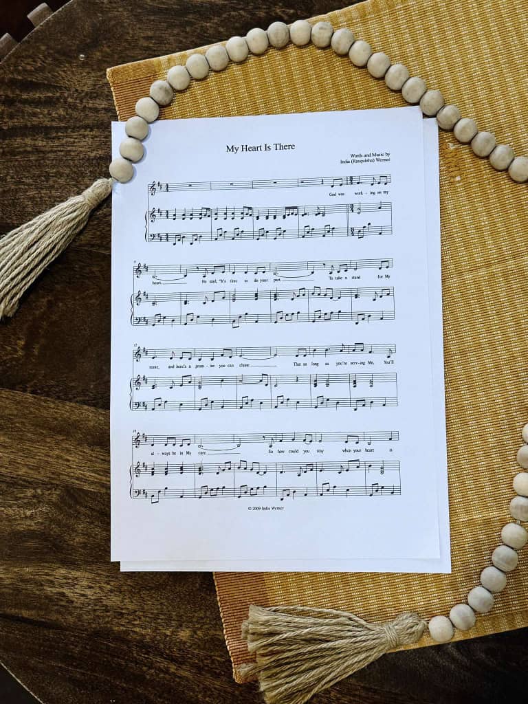 Sheet music to "My Heart is There" by Lois and India laying on a table with a beige table placemat and a strand of beads