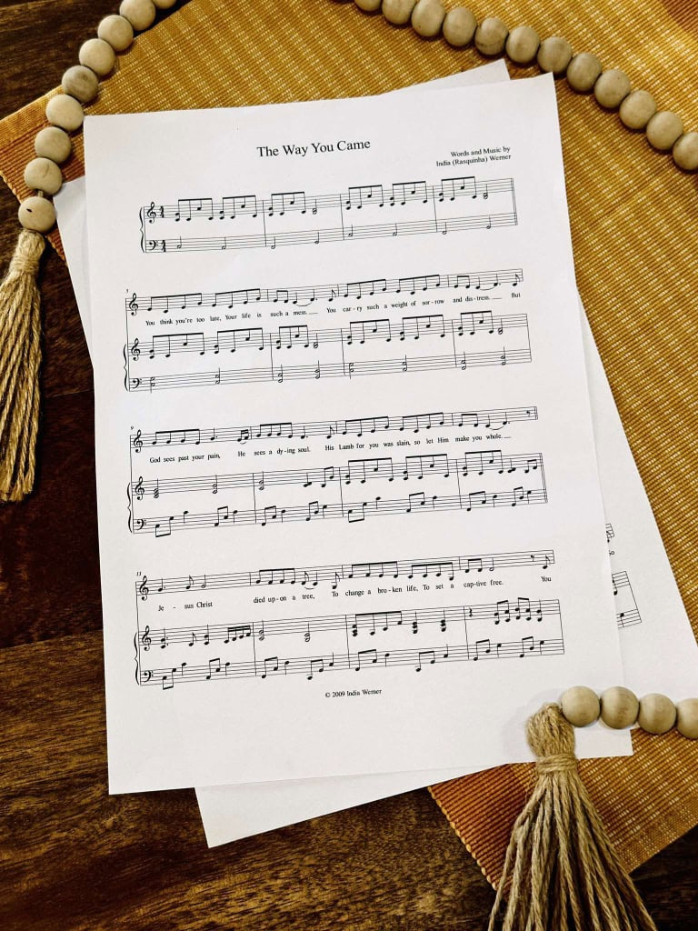 The sheet music to "The Way You Came" by Lois and India laying on a table with a beige placemat and a strand of beads.