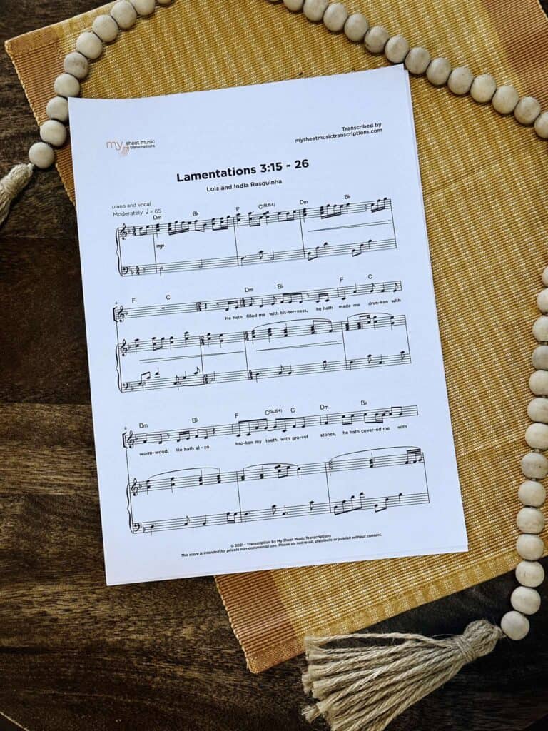 Sheet music to "Lamentations 3:15-26" laying on a table with a yellow placemat and beads.